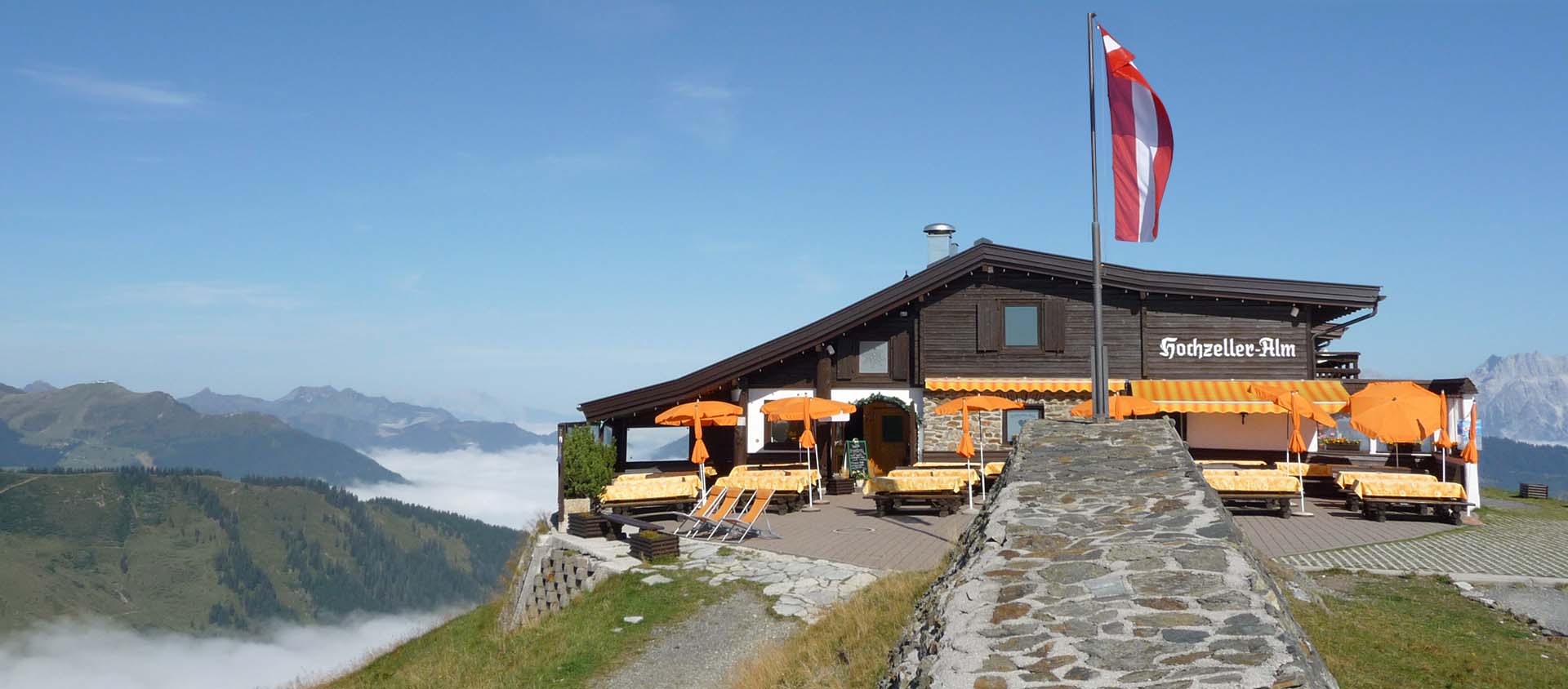 Terrasse der Hochzeller-Alm mit Sonnenschirmen und österreichischer Fahne